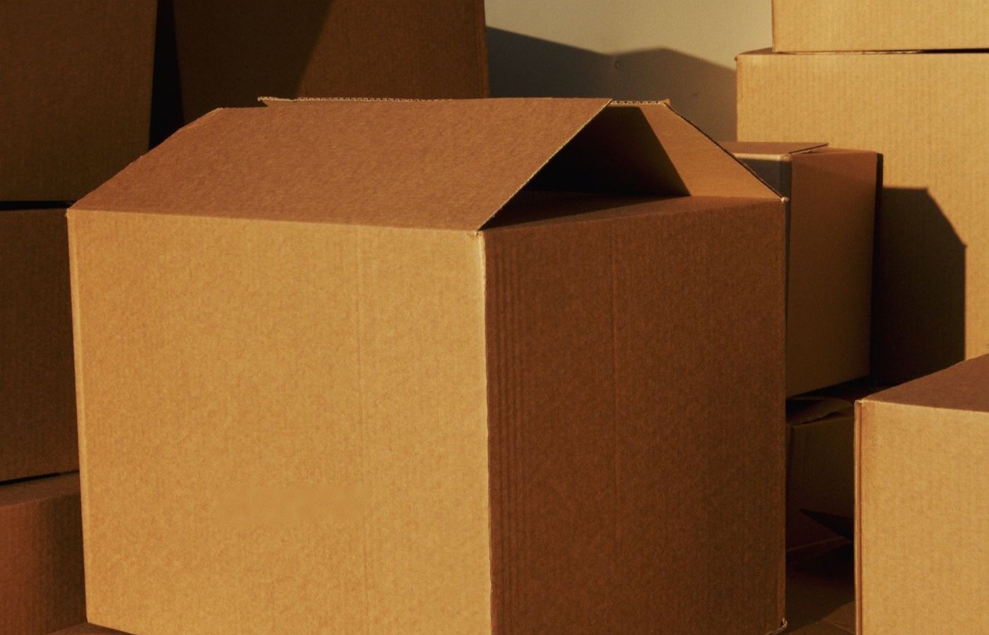 Stacked brown cardboard shipping cartons in warm light, like the supplier cartons that travel from Alibaba sellers in China to buyers in Dhaka