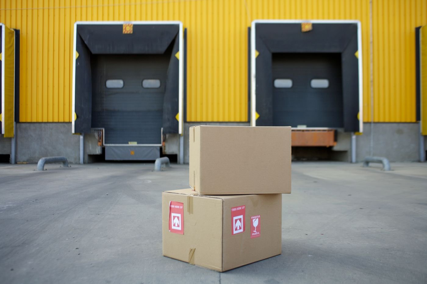 Two cardboard cartons in front of warehouse loading docks, representing per-kg cargo shipping from China to Bangladesh