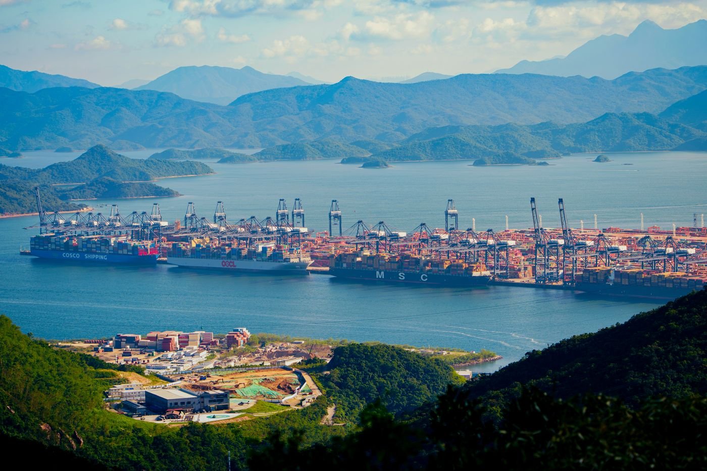 Container ships loading at a large Shenzhen container port surrounded by green hills, the sea route used for cargo from Shenzhen to Chattogram and Dhaka